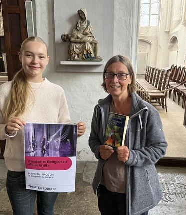 Zwei Frauen stehen mit einem Plakat in einer Kirche.