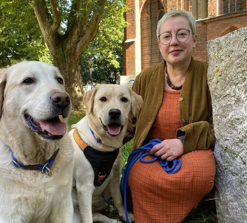 Eine Frau und zwei Hunde sitzen vor einer Kirche