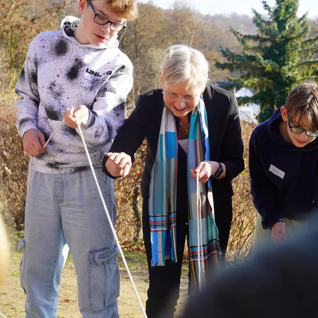 Eine Frau steht mit zwei Jugendlichen konzentriert zusammen und zieht an Seilen.