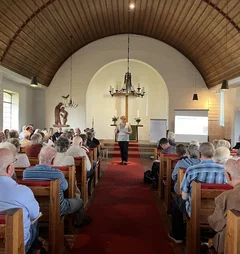 Blick in eine voll besetzte Kirche mit Holzdecke.