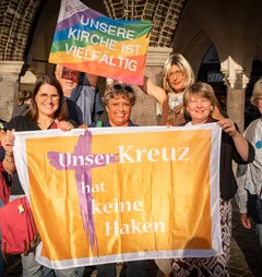 Gruppe von lächelnden Menschen hält zwei bunte Fahnen