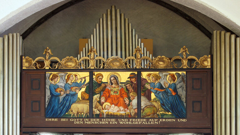 Die Orgelpfeifen einer Orgel, vor der mittleren Orgelpfeifenreihe ist ein altes Gemälde von der Geburt Jesus Christus zu sehen.