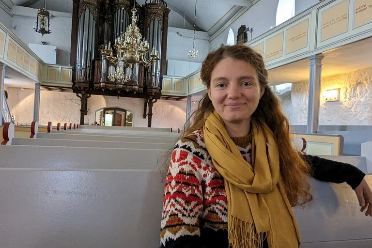 Junge Frau sitzt auf einer Kirchenbank und lächelt in die Kamera.