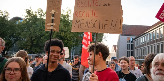 Zwei junge Männer halten Demoschilder und lächeln einander an.