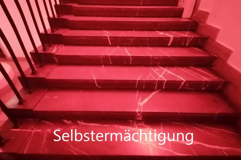 rote Treppenstufen mit Schrift auf unterster Stufe: Selbsermächtigung