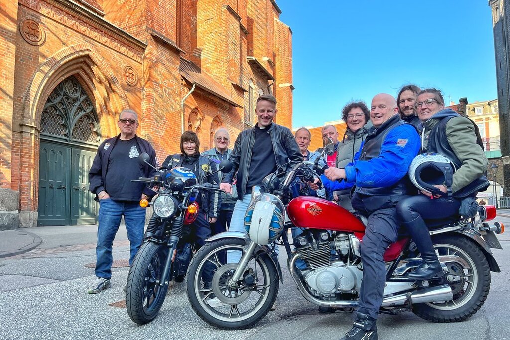 Eine Gruppe Menschen stehen mit zwei Motorrädern vor einer Kirche. 