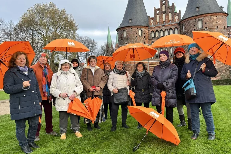 Eine Gruppe von Frauen steht mit orangenen Schirmen vor dem Holstentor. 