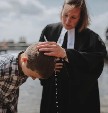 Eine Pastorin tauft einen Jungen im Wasser.