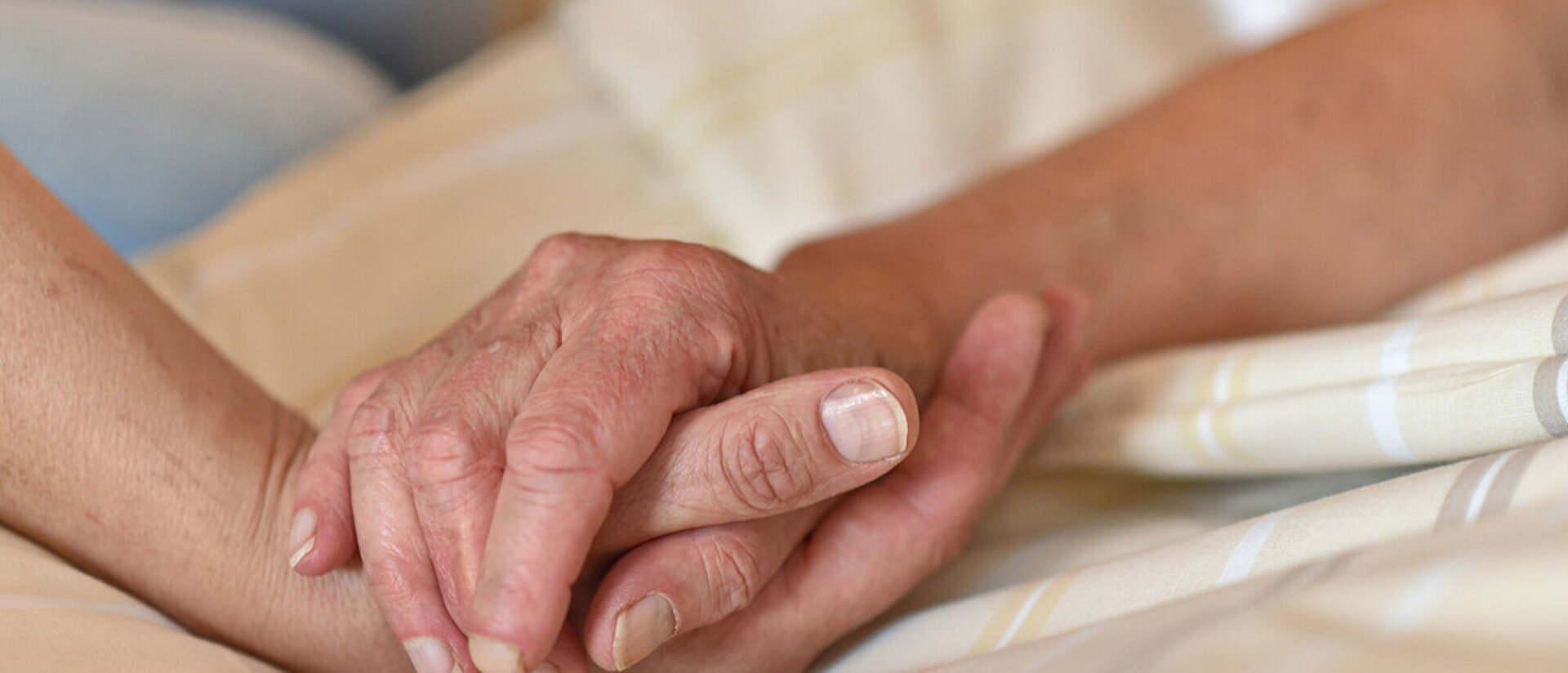 zwei Hände halten einander und liegen auf einer Bettdecke