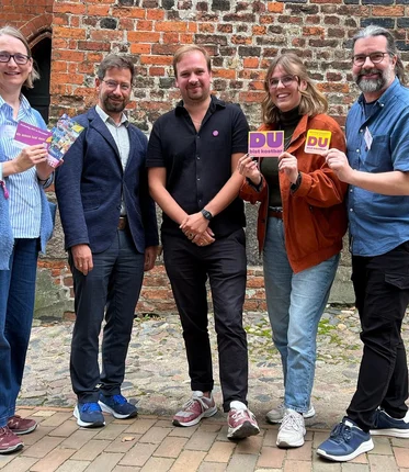 Fünf Menschen  schauen fröhlich in die Kamera