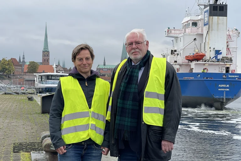 Zwei Menschen vor einem Schiff. 