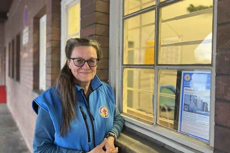 Eine Frau in einer blauen Weste steht an einem Fenster und lächelt.