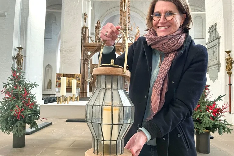 Eine Frau steht mit einem Windlicht in einer Kirche. 