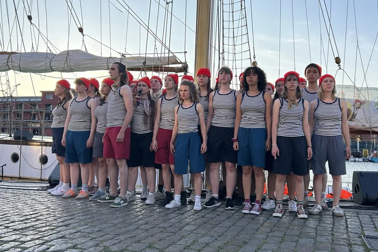 Eine Gruppe junger Menschen steht eng zusammen vor einem Segelschiff.