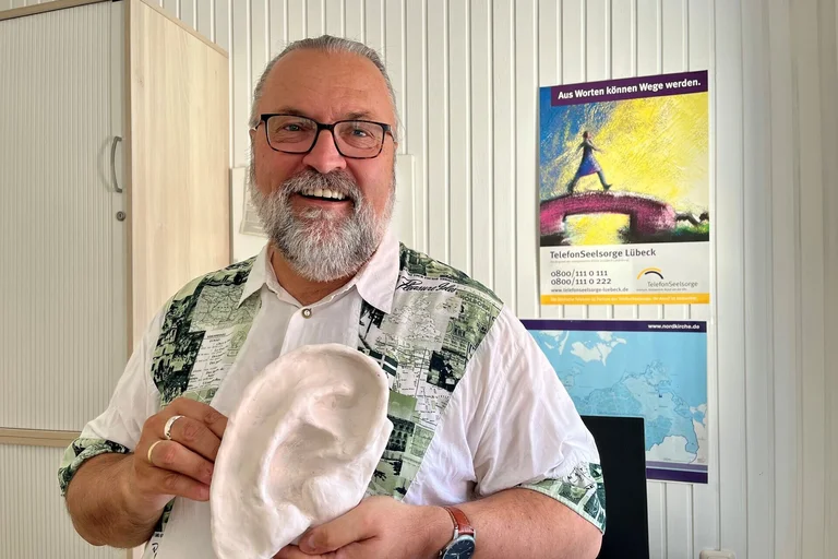 Mann steht mit Gipsohr in der Hand da und lächelt in die Kamera.