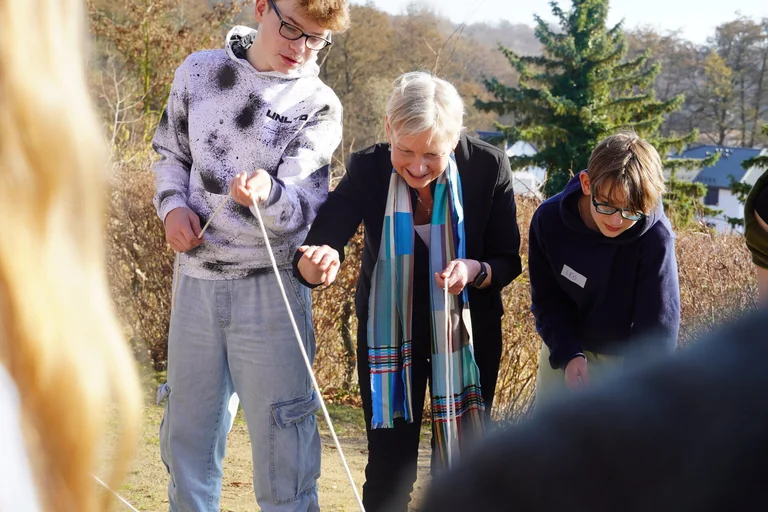 Eine Frau steht mit zwei Jugendlichen konzentriert zusammen und zieht an Seilen.