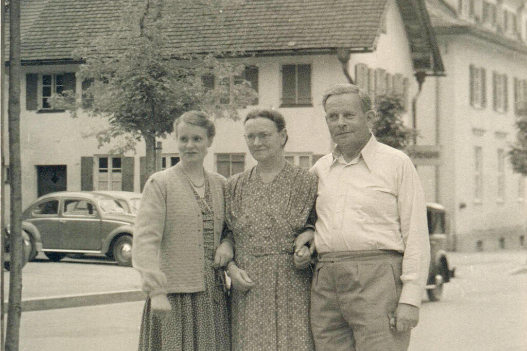 Ein historisches Foto. Drei Menschen sind zu sehen. Sie stehen eingeharkt nebeneinander.