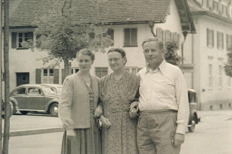 Ein historisches Foto. Drei Menschen sind zu sehen. Sie stehen eingeharkt nebeneinander.