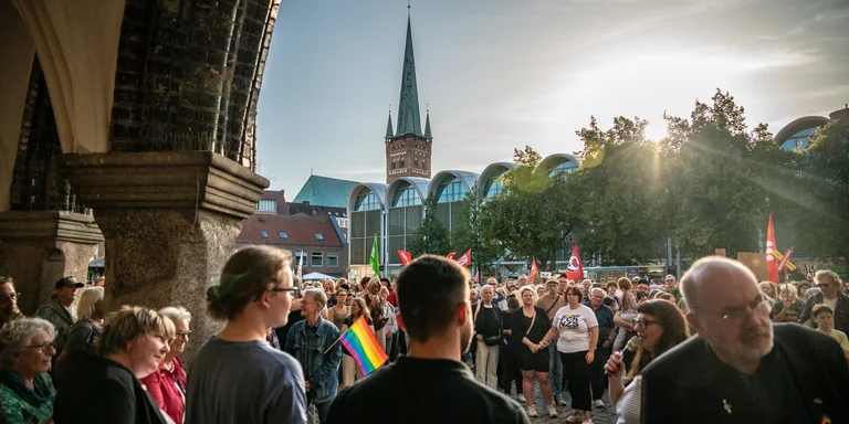 Blick durch Arkaden auf den sonnenbeschienenen Marktplatz in Lübeck mit Demobesuchenden