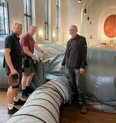Drei Männer stehen vor den mit Folie verhüllten Kirchenbänken.
