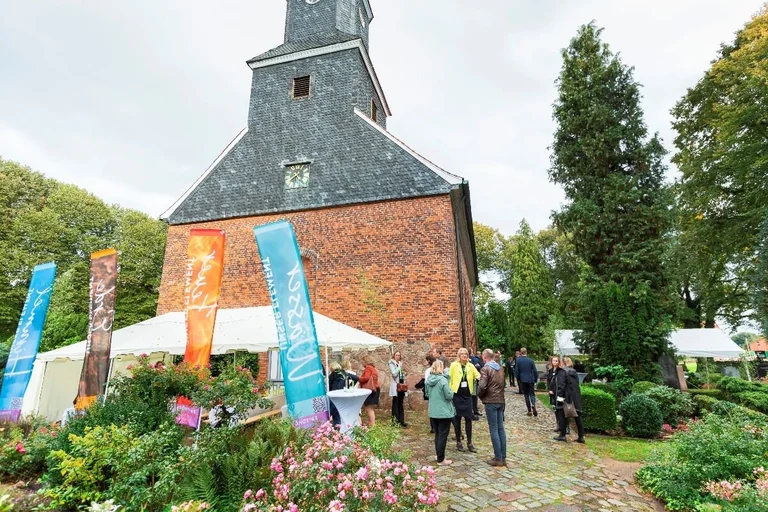 Eine Kirche, Menschen vor der Kirche, Fahnen und ein Pagodenzelt.