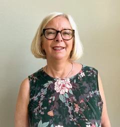 Eine Frau mit grauen kinnlangen Haaren und Brille lächelt in die Kamera.