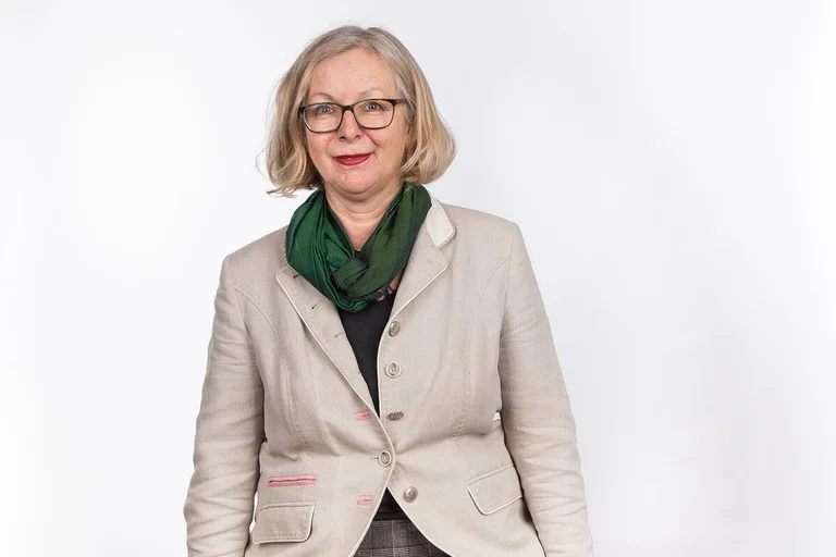 Eine Frau steht vor einer weißen Leinwand und blickt in die Kamera. 