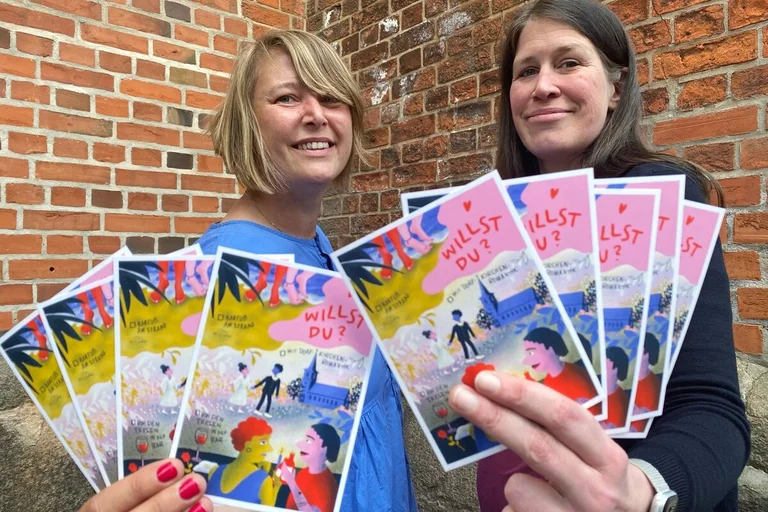 Zwei Frauen halten Postkarten in die Kamera