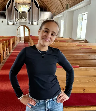 Junge Frau steht in einer Kirche und lächelt in die Kamera.