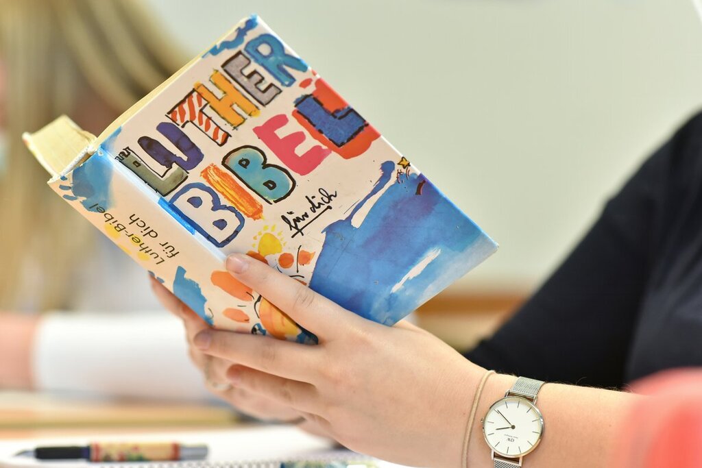 Hände halten eine aufgeschlagene bunt gestaltete Bibel