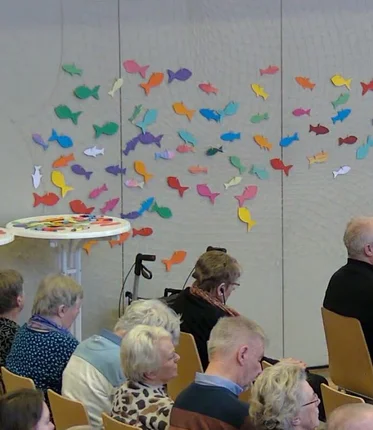 Bunte Papierfische an einer Wand, davor sitzen mehrere Personen