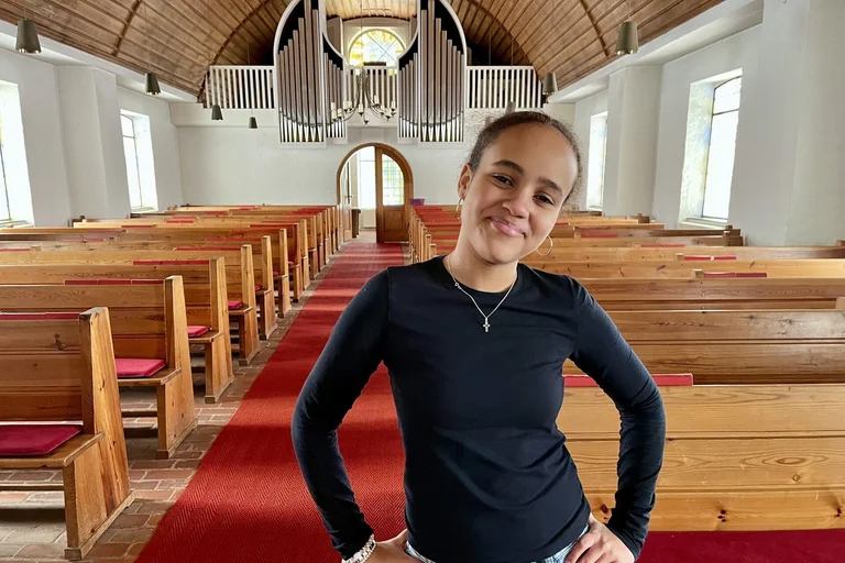 Junge Frau steht in einer Kirche und lächelt in die Kamera.