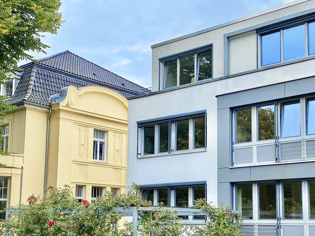 Alt- und Neubau der Kirchenkanzlei - Auf der linken Seite der Altbau mit gelber Fassade und dunklem Dach, rechts der Neubau in Grautönen und Flachdach