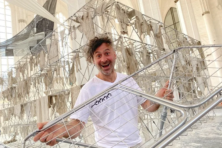 Mann hält einen Wäscheständer in den Händen vor einer Installation in einer Kirche. 