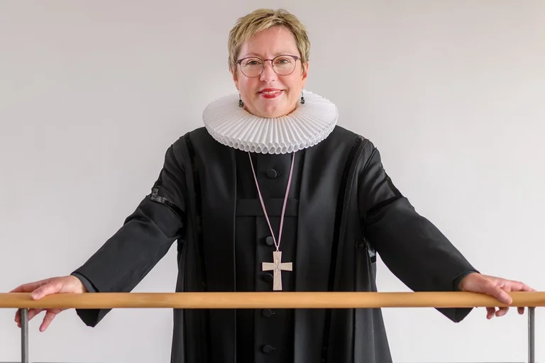 Eine Frau im Talar, mit weißem Kragen und goldenem Kreuz schaut freundlich in die Kamera.