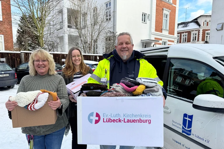 Drei Personen stehen mit Kartons vor einem Auto 