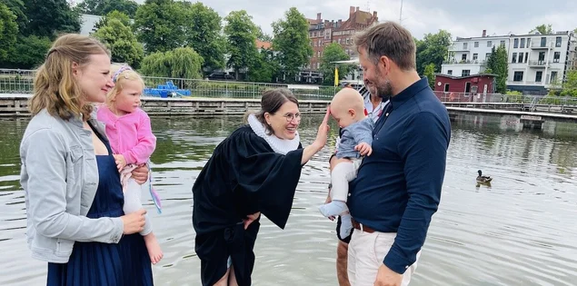 Nach Töchterchen Eva (vor zwei Jahren) lassen Marlene und Tobias Reinberger Sohnemann Johan von Pastorin Margrit Wegner taufen. Sie alle stehen im Wasser, die Pastorin lächelt und tauft Johan.