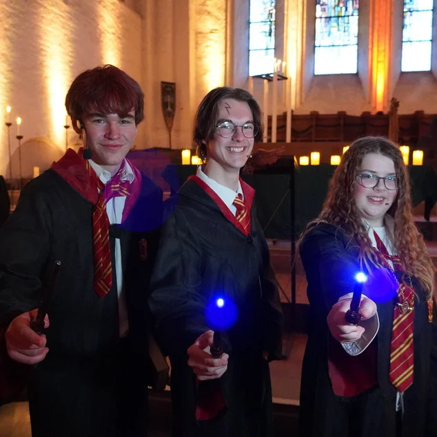 Drei junge Menschen in Verkleidung halten leuchtende Zauberstäbe.