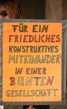 Demobesucherin mit einem Schild mit der Aufschrift "Für ein friedliches konstruktives Miteinander in einer bunten Gesellschaft"