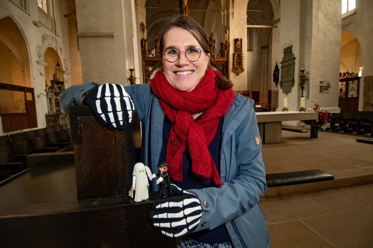 Eine Frau sitzt mit Knochenhandschuhen in einer Kirche