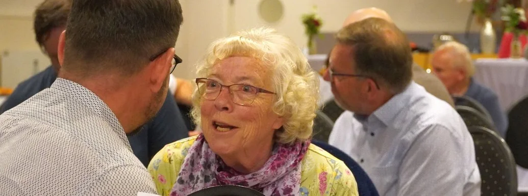 Eine Frau mit grauen Haaren und grünem Oberteil spricht mit einem Mann.