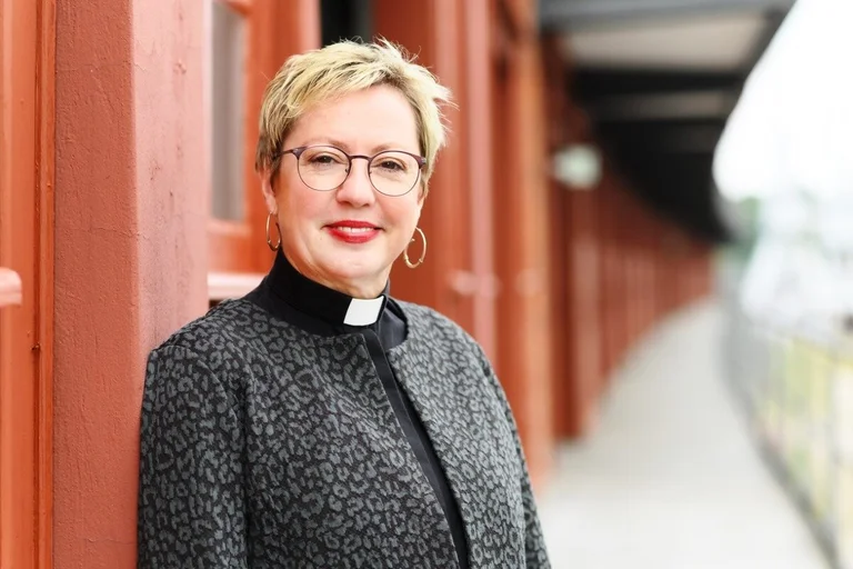 Eine Frau mit Brille, kurzen Haaren schaut freundlich in die Kamera. Sie trägt ein schwarzes Kollarhemd und eine schwarze, in sich gemusterte Jacke.