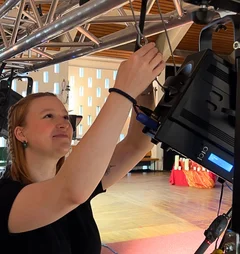 Eine junge Frau arbeitet an einem großen Scheinwerfer.