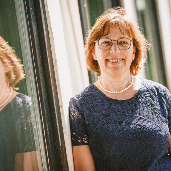Eine Frau lehnt an einem Fenster und lächelt in die Kamera.