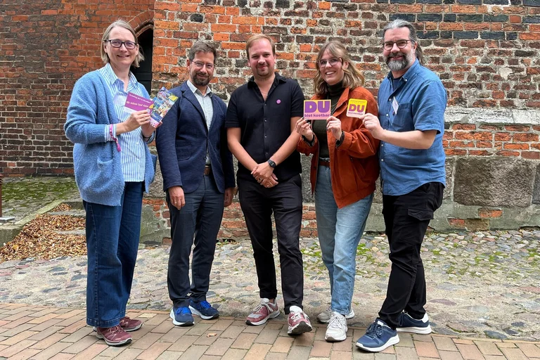 Fünf Menschen  schauen fröhlich in die Kamera