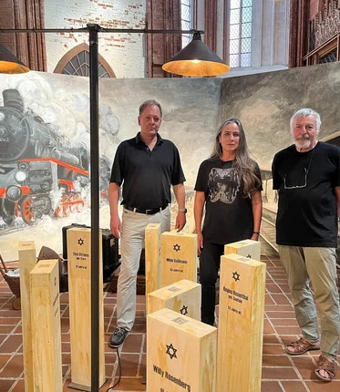 Drei Menschen stehen vor einem Gemälde und hinter einer Kunstinstallation