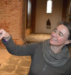 Eine Frau reicht einer kleinen Figur in einer Kirche einen Kugelschreiber.