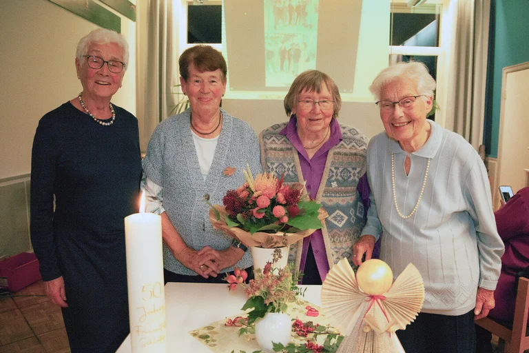 Vier ältere Frauen stehen vor einem geschmückten Tisch und schauen freundlich in die Kamera.