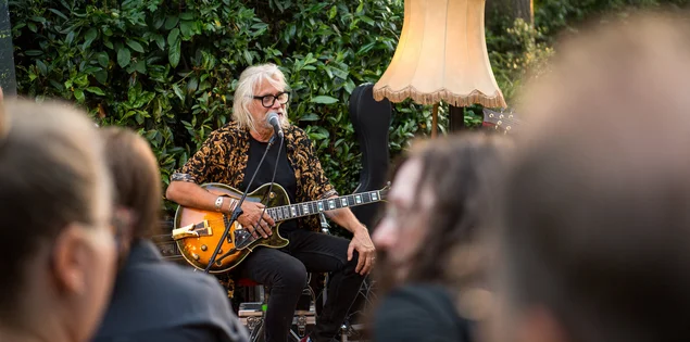 Ein Mann singt und spielt Gitarre vor Publikum im Grünen.