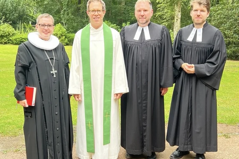 Vier Personen stehen unter freiem Himmel und lächeln in die Kamera. 